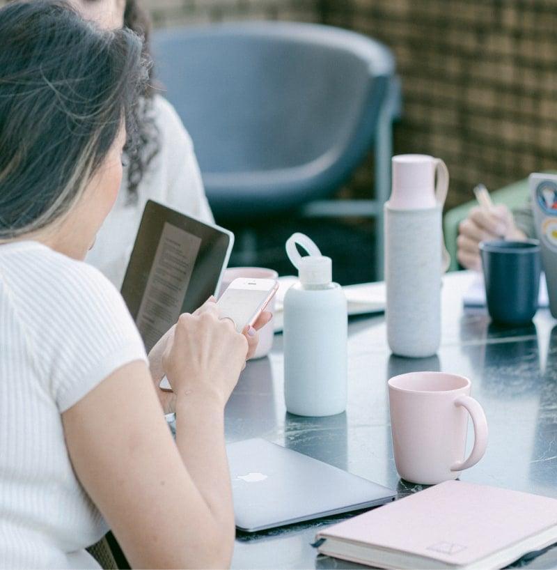 Woman using a mobile device to book a TrustTest demo, with laptop in background showing online exam platform.